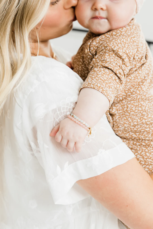 A mother holding a baby shows off her newborn jewelry